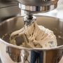 Stand mixer with dough hook attachment kneading bread dough in stainless steel bowl