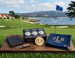 A neatly arranged set of personalized golf gifts including custom golf balls, an engraved ball marker, and a monogrammed towel on a golf course