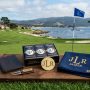 A neatly arranged set of personalized golf gifts including custom golf balls, an engraved ball marker, and a monogrammed towel on a golf course