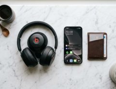 Premium black over-ear headphones resting on a modern wooden desktop stand.