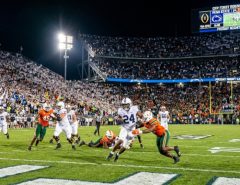 College football players competing in the first round of the 2026–27 College Football Playoff on a packed campus stadium field under the Friday night lights