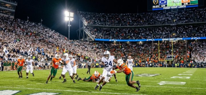 College football players competing in the first round of the 2026–27 College Football Playoff on a packed campus stadium field under the Friday night lights