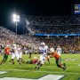 College football players competing in the first round of the 2026–27 College Football Playoff on a packed campus stadium field under the Friday night lights