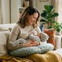 Mother holding her baby using a curved nursing pillow on a sofa.